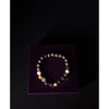 Multicolored beaded bracelet on a purple velvet box with 'maharishi' branding.