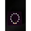 Bracelet with white beads on a purple stand against a black background