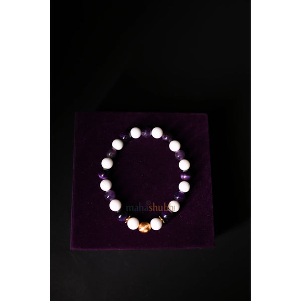 Bracelet with white beads on a purple stand against a black background