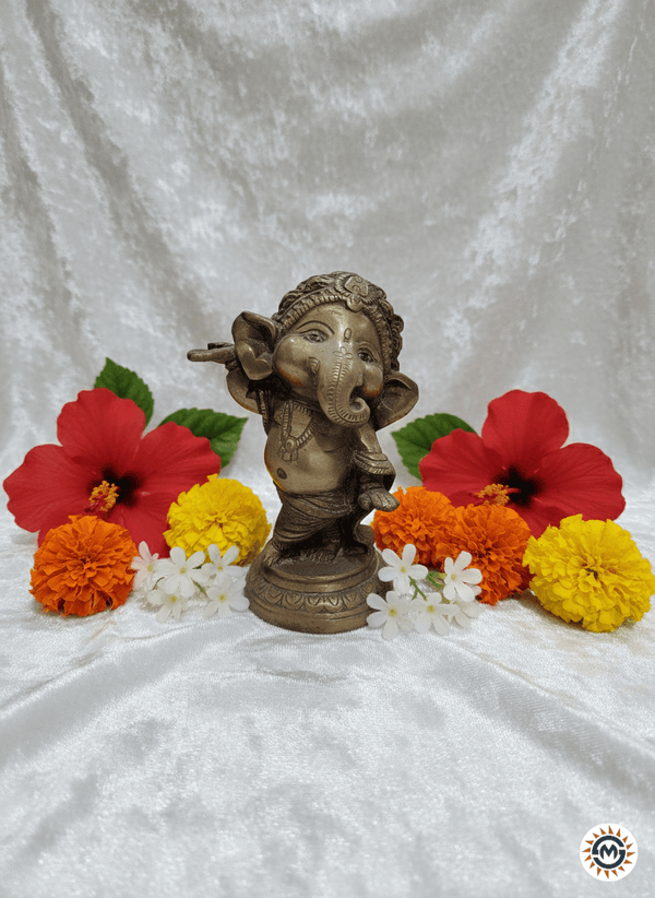 Detailed brass sculpture of Bala Ganapati, the infant Ganesha, seated with a sweet modak and fruit, showcasing intricate traditional Indian metalwork and golden luster.