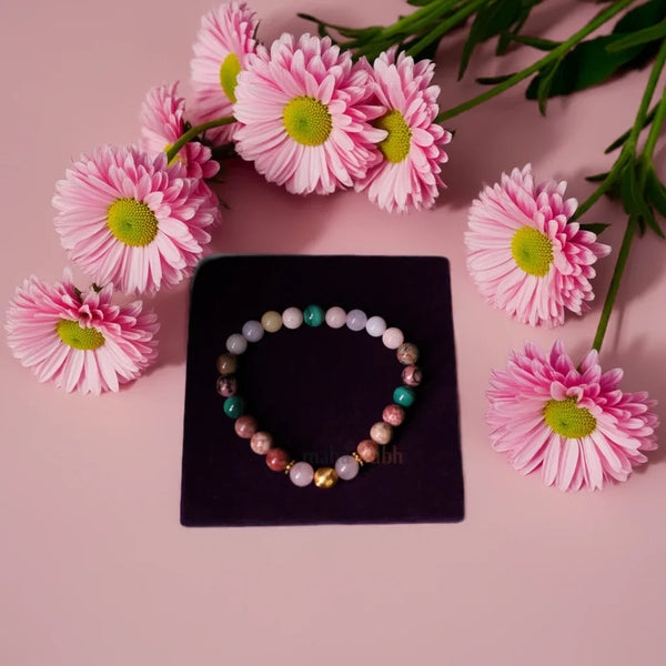 Colorful beaded bracelet on a black stand with pink flowers around it on a pink background