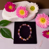 Colorful beaded bracelet on a black card with pink and white flowers and green leaves on a light surface.