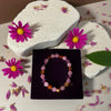 Bracelet on a black box with pink flowers and a green leaf on a textured surface.