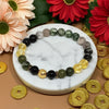 Bracelet with green, black, and gold beads on a marble surface with flowers and coins around.