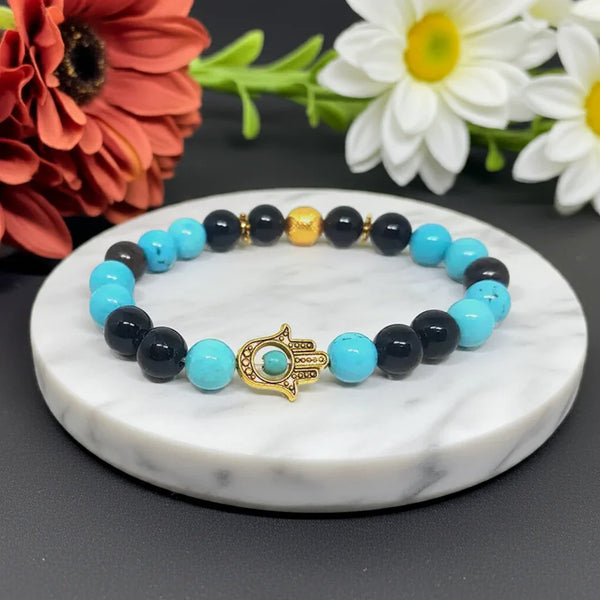 Beaded bracelet with gold hamsa charm on a marble coaster with flowers in the background