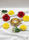 Brass diya lamp surrounded by red roses, yellow marigold flowers, and white daisies on white fabric