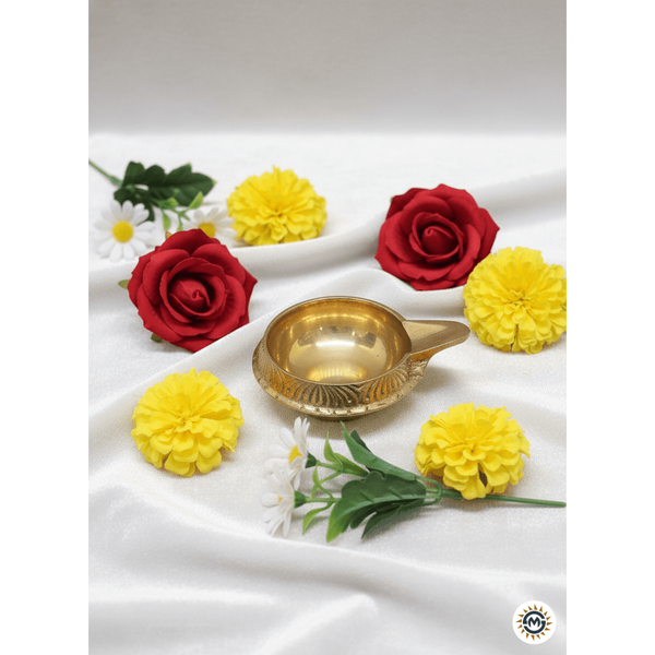 Brass diya lamp surrounded by red roses, yellow marigold flowers, and white daisies on white fabric