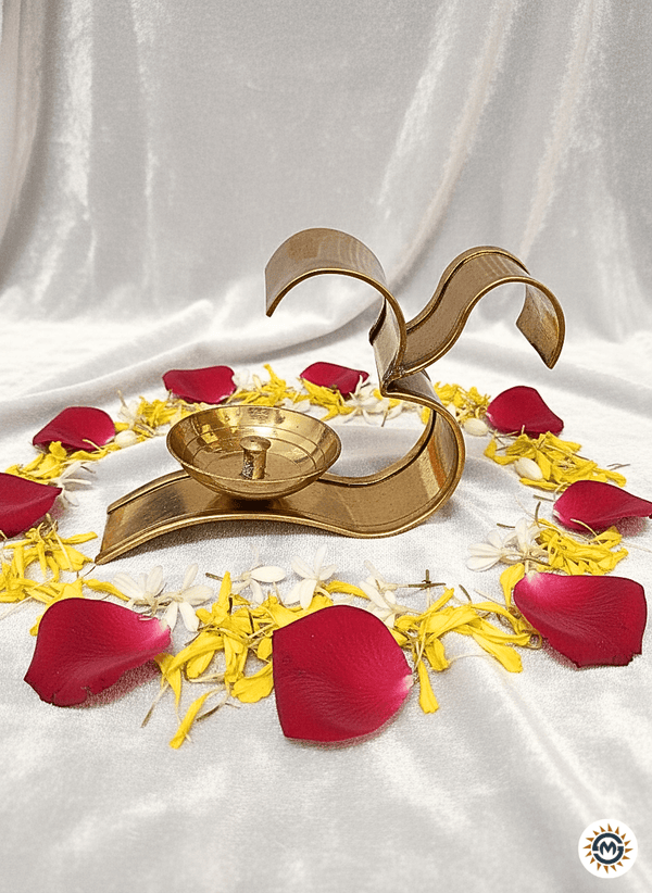 brass Om diya candle holder surrounded by red rose petals and yellow-white flower petals on white satin