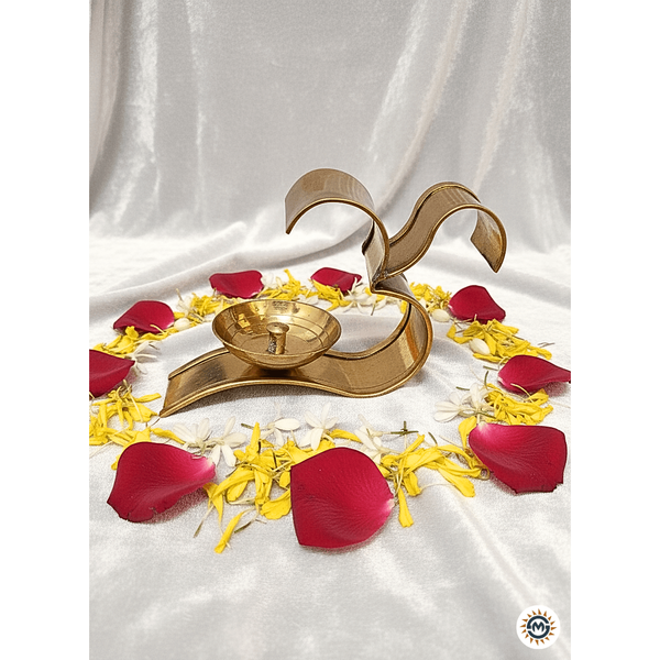 brass Om diya candle holder surrounded by red rose petals and yellow-white flower petals on white satin