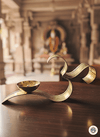 Brass OM diya lamp on wooden table inside traditional Indian temple with blurred deity statue in background