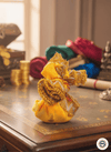 Decorative yellow and gold item on a wooden surface with colorful fabrics in the background