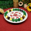 Colorful beaded bracelet on a white plate with flowers, surrounded by green leaves and gold coins.