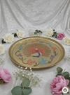 Decorative tray with peacock design surrounded by flowers on a white fabric background