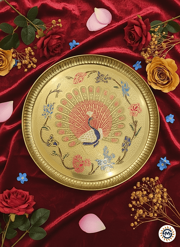 Decorative gold plate with peacock design on a red fabric background with flowers.