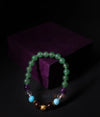Beaded bracelet with green, purple, and gold beads on a dark background