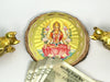 A gold-colored Yantra featuring an image of Goddess Lakshmi with a lotus flower, surrounded by two golden figurines, against a white background with a denomination note and a coin.