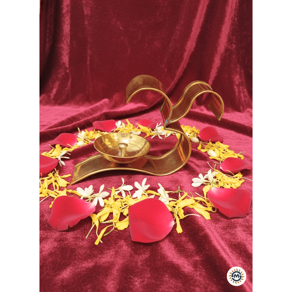 Golden Om diya lamp on red velvet with arranged red rose, yellow and white flower petals