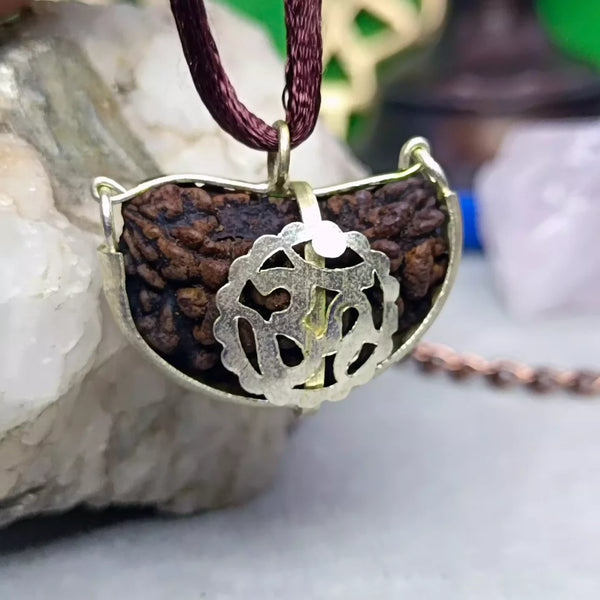 A kidney-shaped Rudraksha bead with a decorative metal holder attached to a cord, typically used as a spiritual accessory.