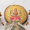 A gold-colored Yantra featuring an image of Goddess Lakshmi with a lotus flower, surrounded by two golden figurines, against a white background with a denomination note and a coin.