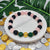 Colorful beaded bracelet on a white surface with coins and green leaves in the background