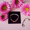 Colorful beaded bracelet on a black card with pink flowers around it