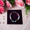 Multicolored beaded bracelet on a dark purple card with pink roses and green leaves in the background.