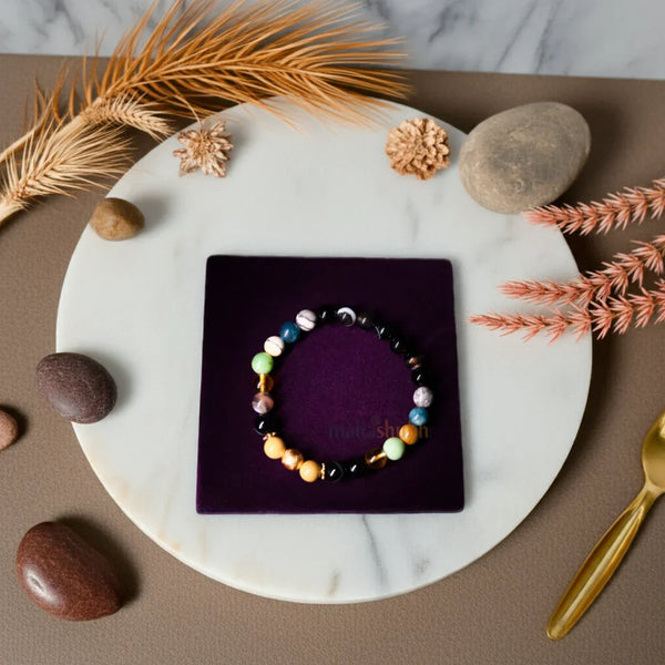 Colorful beaded bracelet on a purple square with decorative elements like stones and plants on a marble surface.