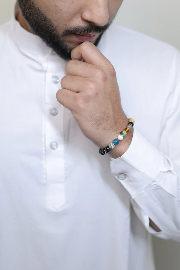 Person wearing a white shirt with a colorful beaded bracelet on a plain background