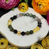 Bracelet with green and black beads and gold coins on a marble surface with flowers and more gold coins around.