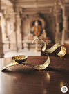 Brass OM diya lamp on wooden table inside traditional Indian temple with blurred deity statue in background