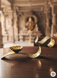 Brass OM diya lamp on wooden table inside traditional Indian temple with blurred deity statue in background