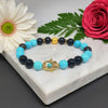 Bracelet with blue and black beads and a gold Hamsa charm on a marble surface with flowers.