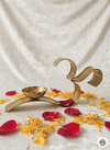 Brass Om-shaped diya lamp surrounded by red rose and yellow flower petals on white fabric