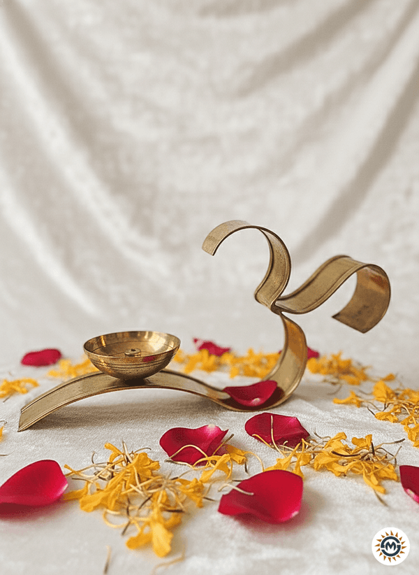 Brass Om-shaped diya lamp surrounded by red rose and yellow flower petals on white fabric