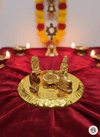Golden Hindu puja plate with Lingam, Nandi, deities on red velvet cloth, surrounded by lit oil lamps and marigold garland