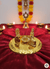 Golden Hindu puja plate with Lingam, Nandi, deities on red velvet cloth, surrounded by lit oil lamps and marigold garland
