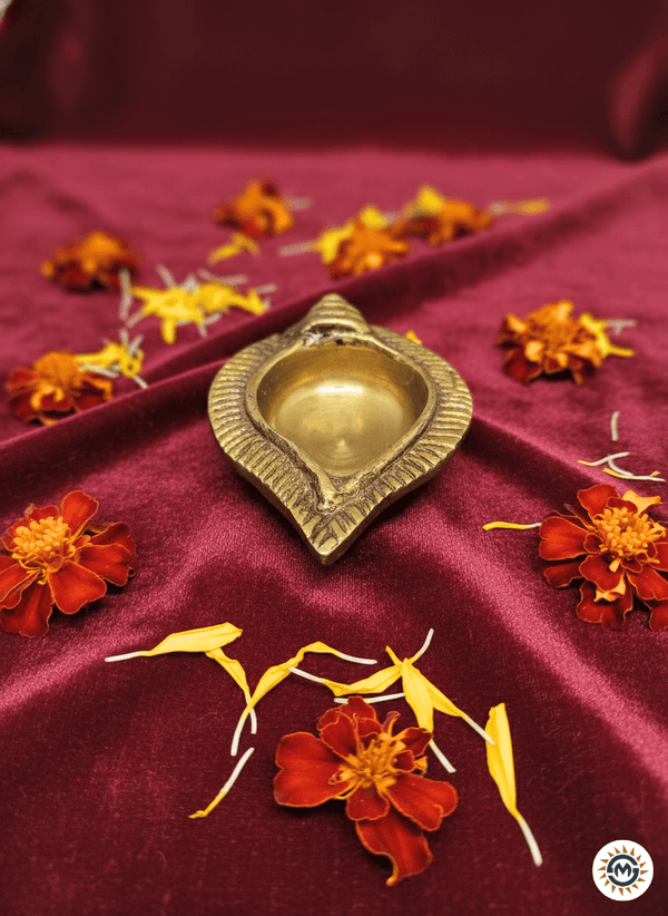 Traditional brass oil lamp on maroon velvet fabric surrounded by red and yellow marigold petals
