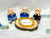 A collection of small statues wearing blue robes, seated around a wooden disc with a Yellow Citrine Bracelet on it, surrounded by various colorful gemstones.
