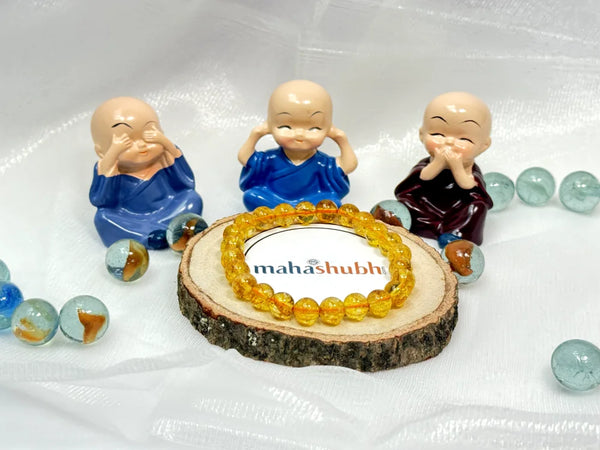 A collection of small statues wearing blue robes, seated around a wooden disc with a Yellow Citrine Bracelet on it, surrounded by various colorful gemstones.
