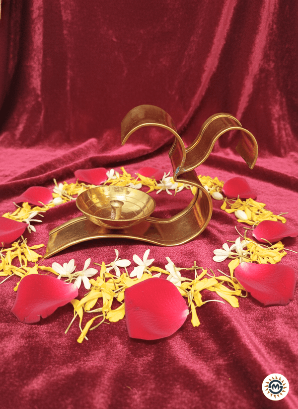 Golden Om diya lamp on red velvet with arranged red rose, yellow and white flower petals